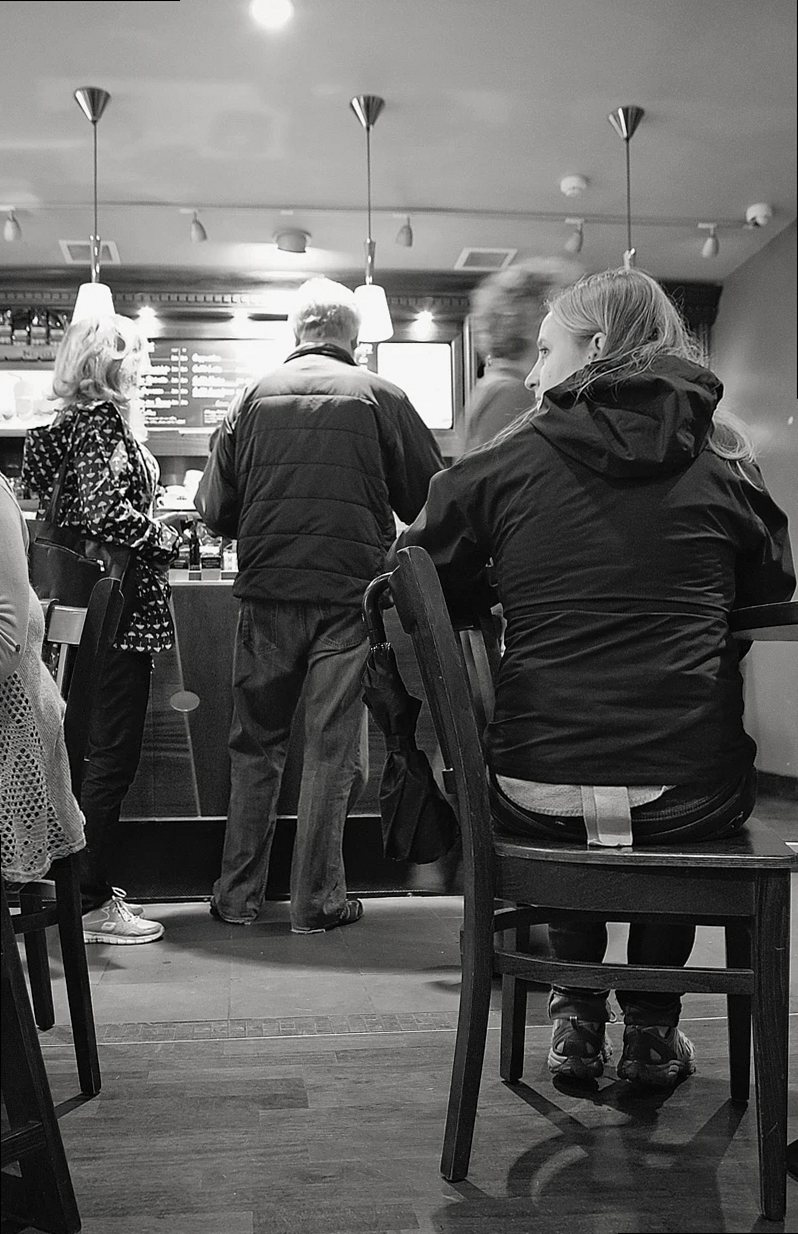 cafetería en blanco y negro, estilo retro, mujer esperando a una amiga, personas haciendo cola